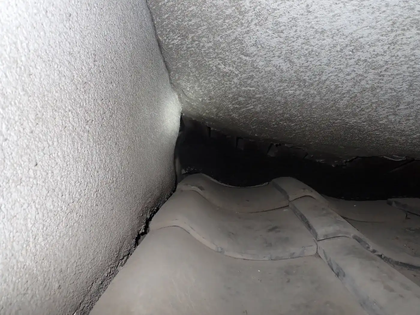 外壁と瓦屋根が接する角で、瓦の奥へ黒い隙間が続いている