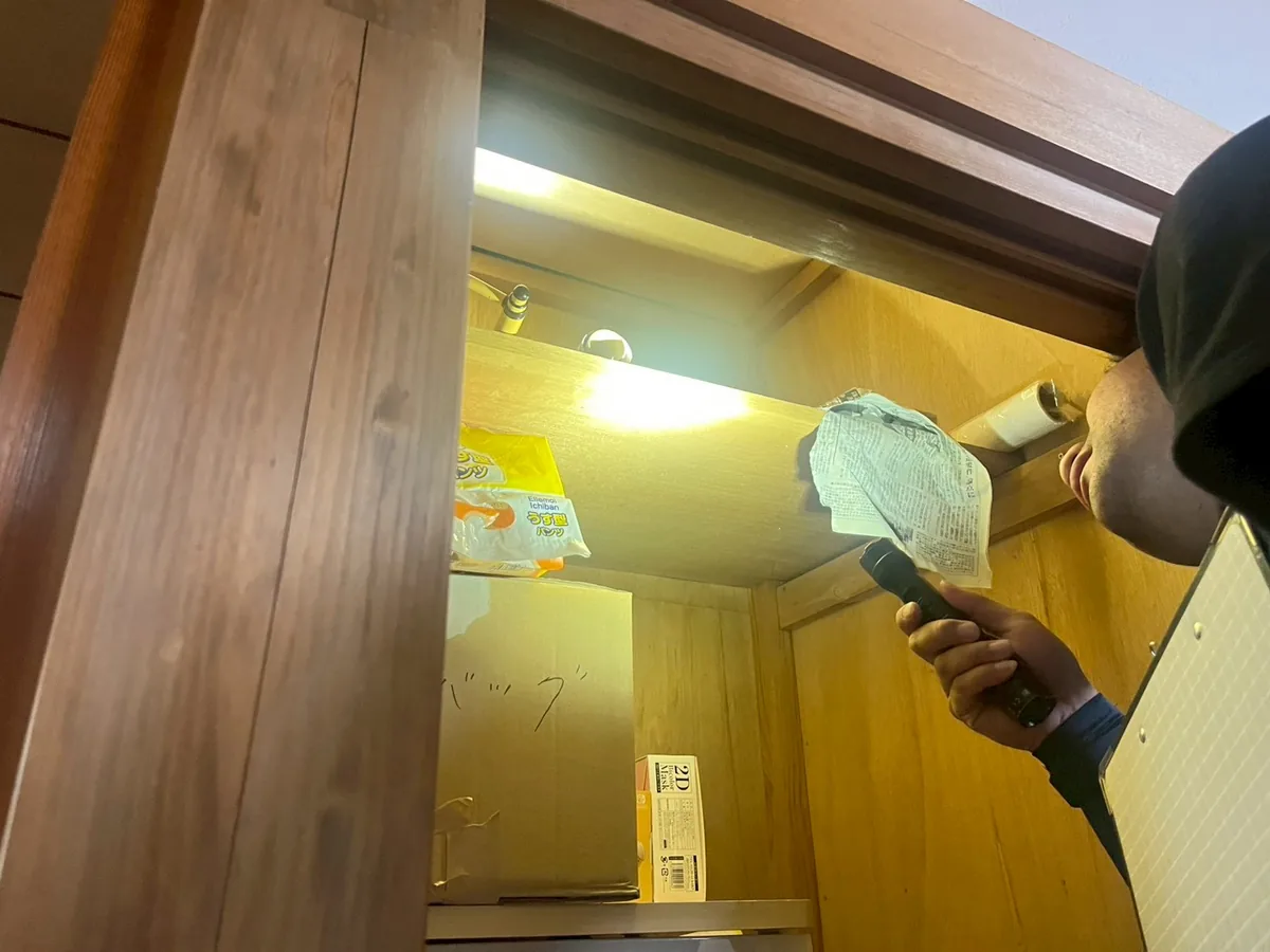 作業員が懐中電灯を手に、収納の上部を照らして奥を点検している場面