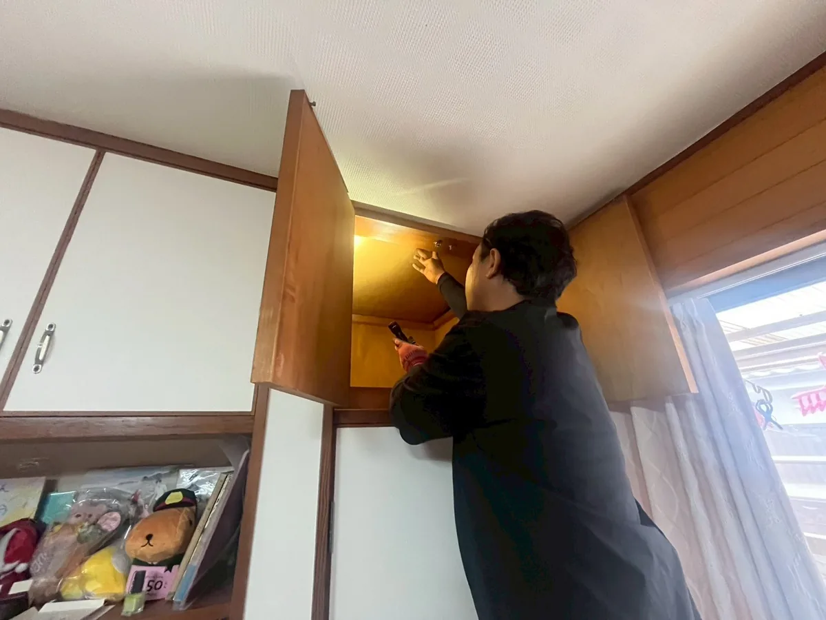 押し入れの上の天袋を開け、ライトで奥を点検する作業員
