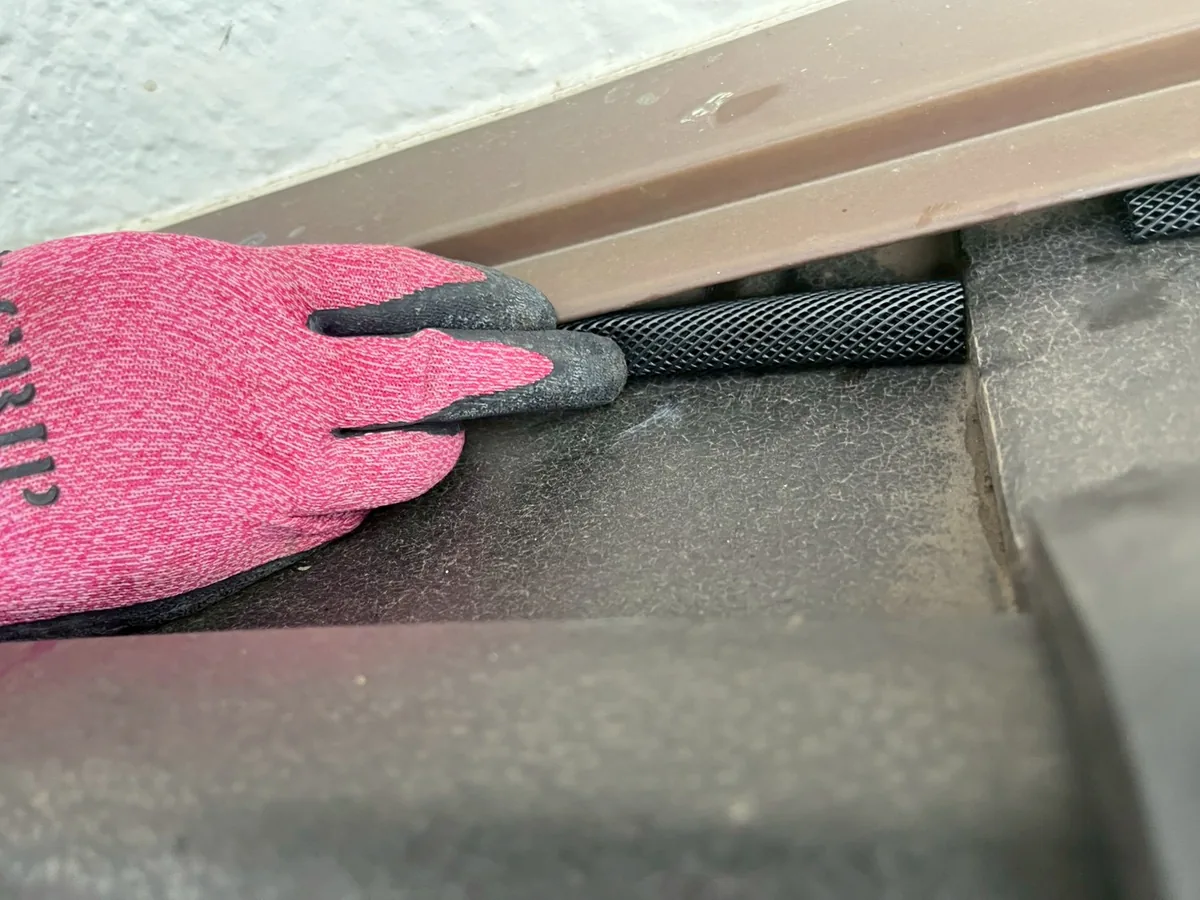 瓦のすき間に押し込んだ黒い筒状の網と、それを手袋の指で押さえる作業