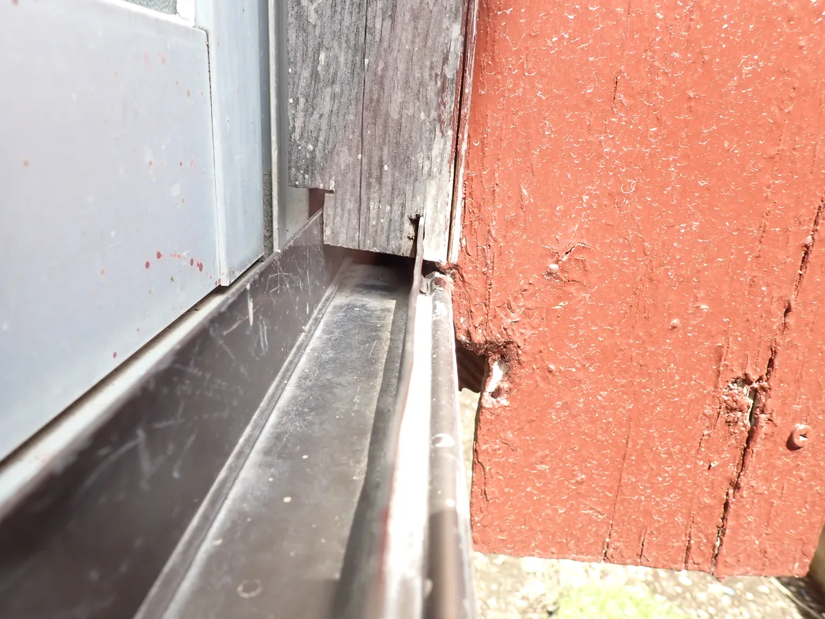 窓枠と赤茶色の木部が接する部分に穴が開いている、外壁の端の傷み