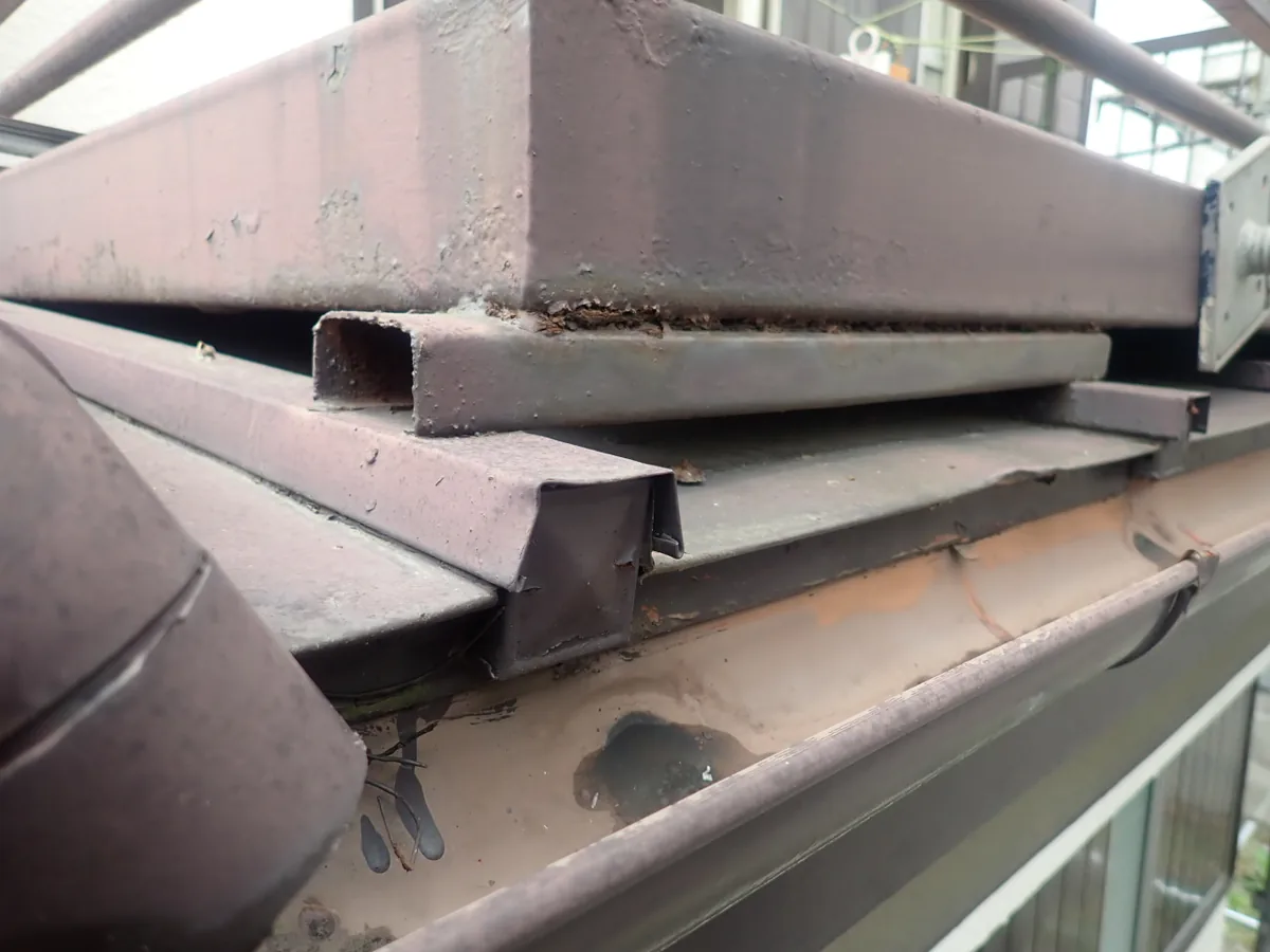 角形の鉄骨と屋根の板金のあいだに細い隙間が続き、その下を雨樋が通る金属屋根の軒先