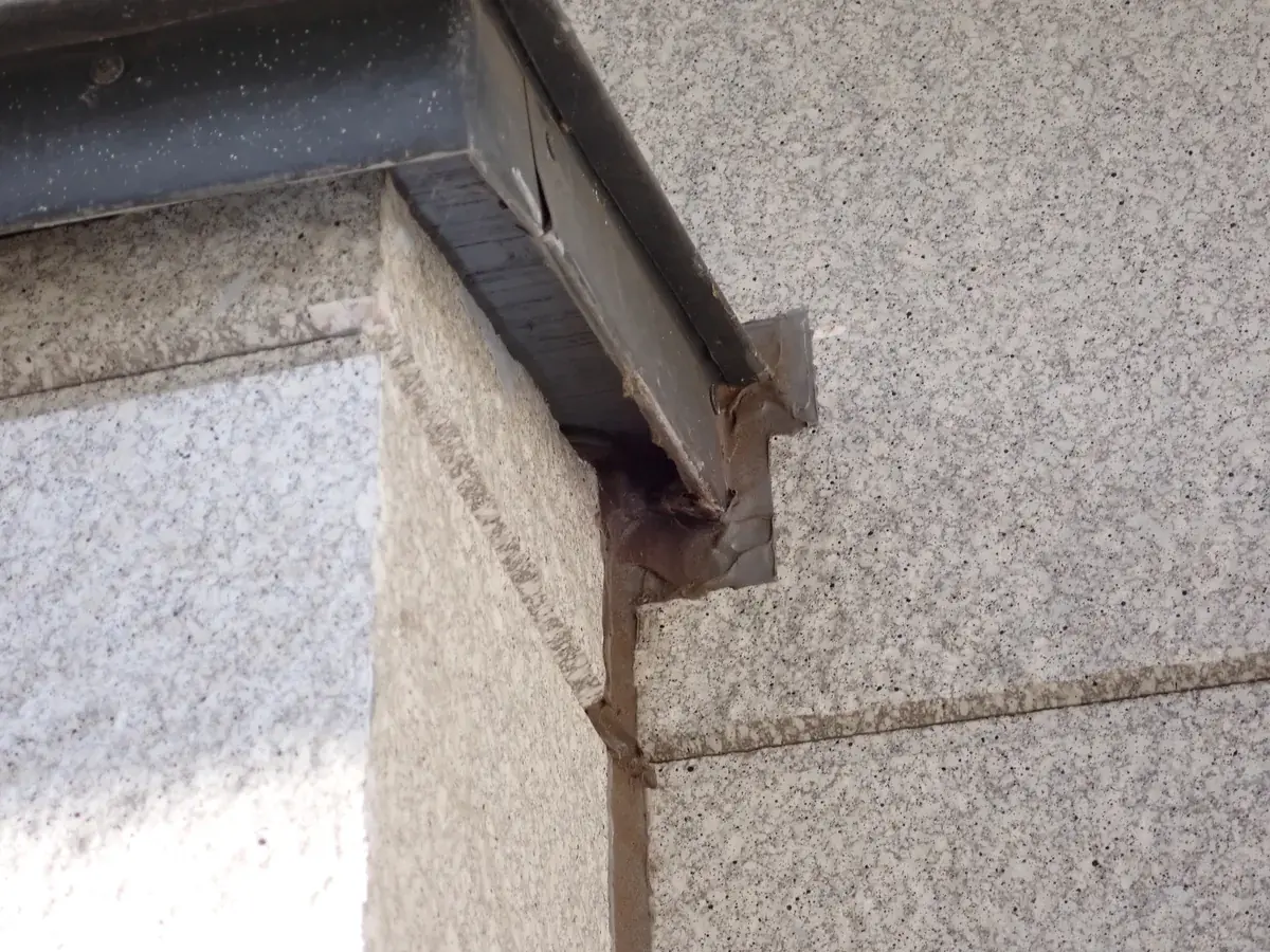 軒と外壁の角が接する水切りの下で、仕上げが欠けた接合部