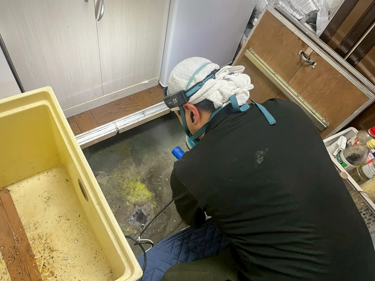 防護マスクを着けた作業員が噴霧器を使い、室内の床まわりを消毒している作業の様子