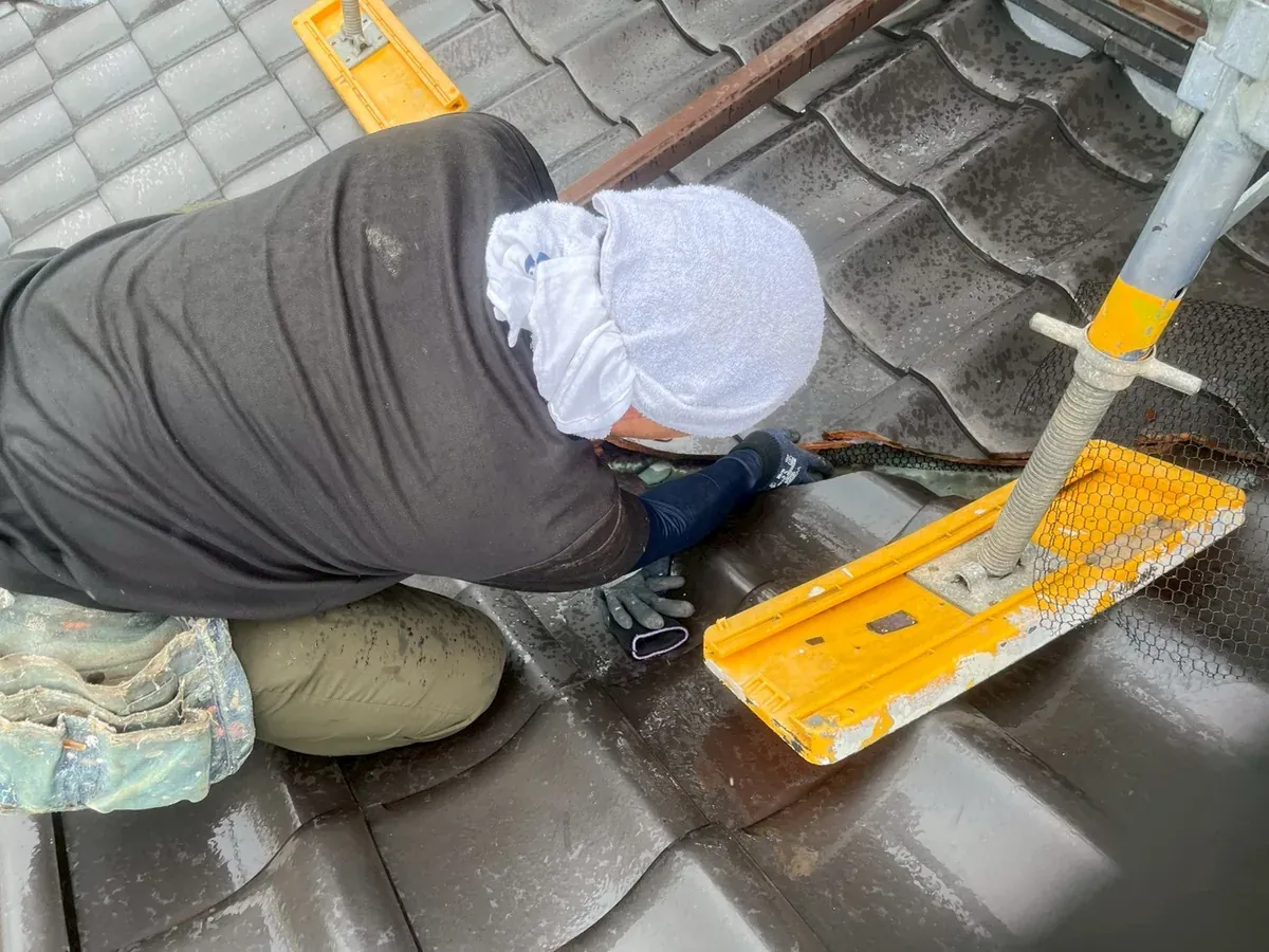 瓦屋根の上で、瓦のすき間に手を入れて作業する職人