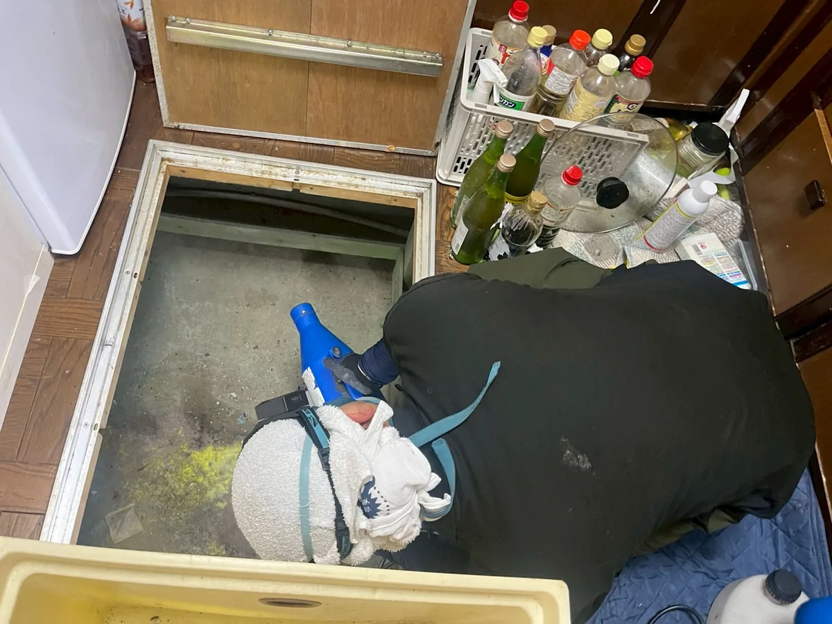 台所の床下点検口から、床下へ薬剤を吹き付けている消毒作業